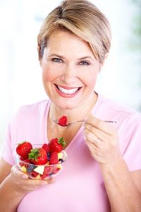 Middle-aged woman eating a bowl of fruit and smiling